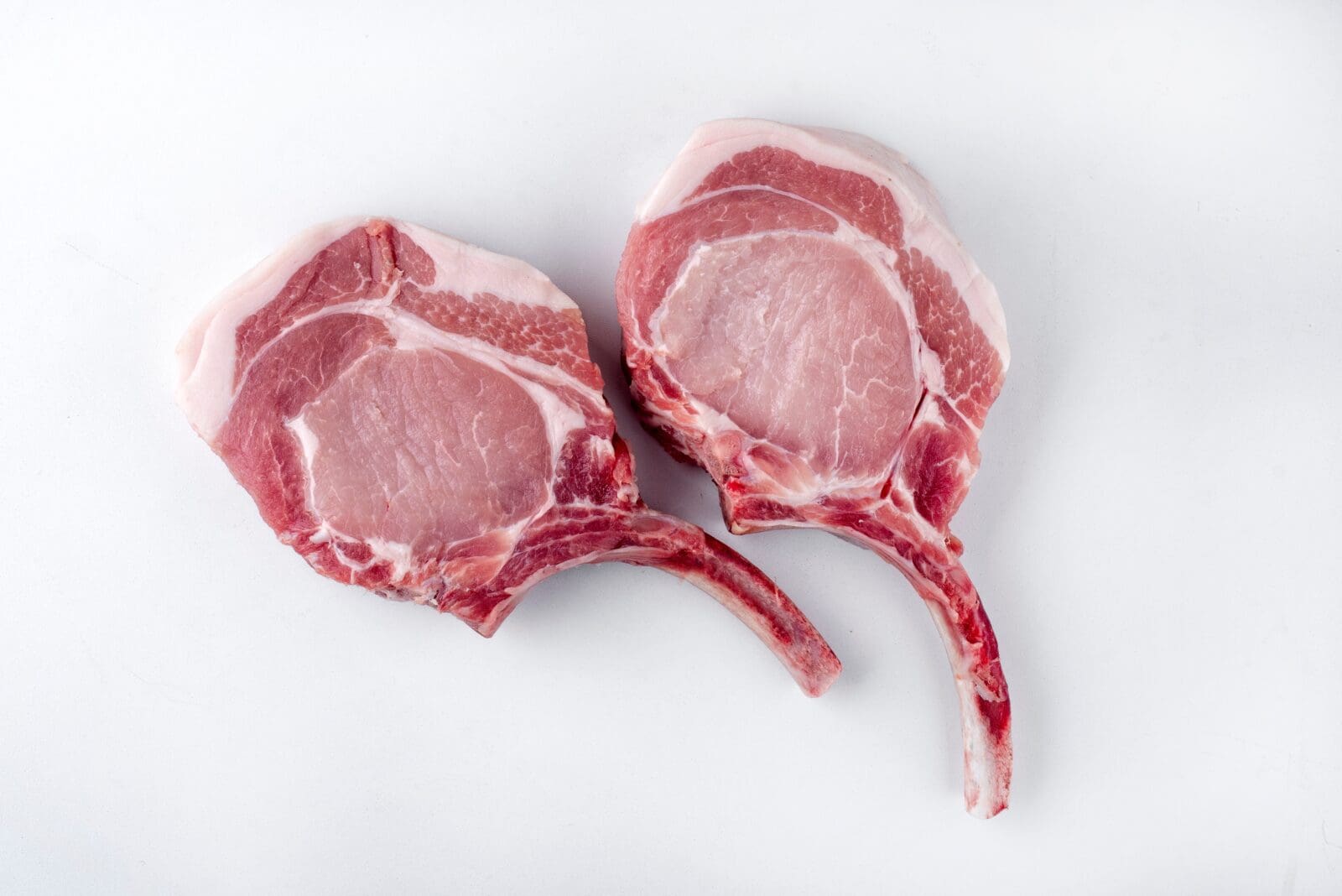 Two raw pork chops with bones displayed on a white surface.