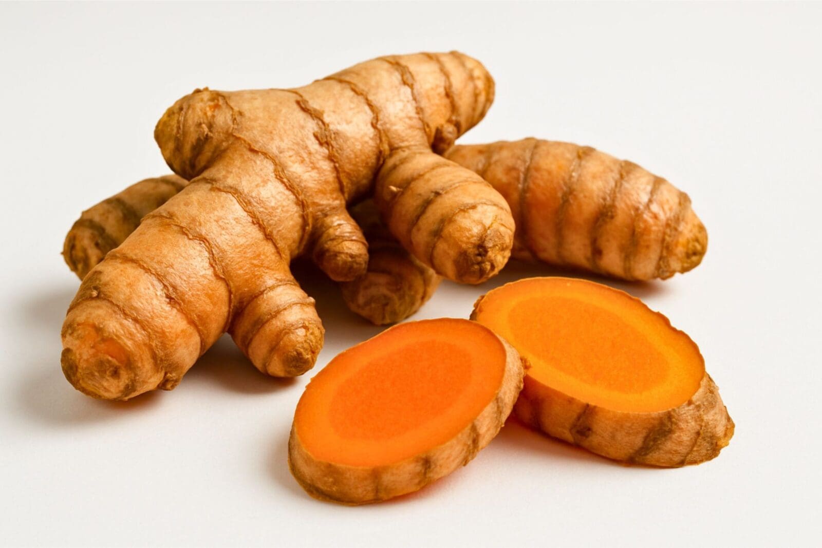 Turmeric roots with rough brown skin and vibrant orange interior, some cut to show inside.