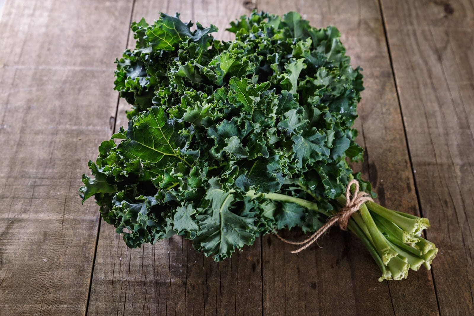 Bunch of fresh, curly kale leaves tied with twine on a wooden surface.