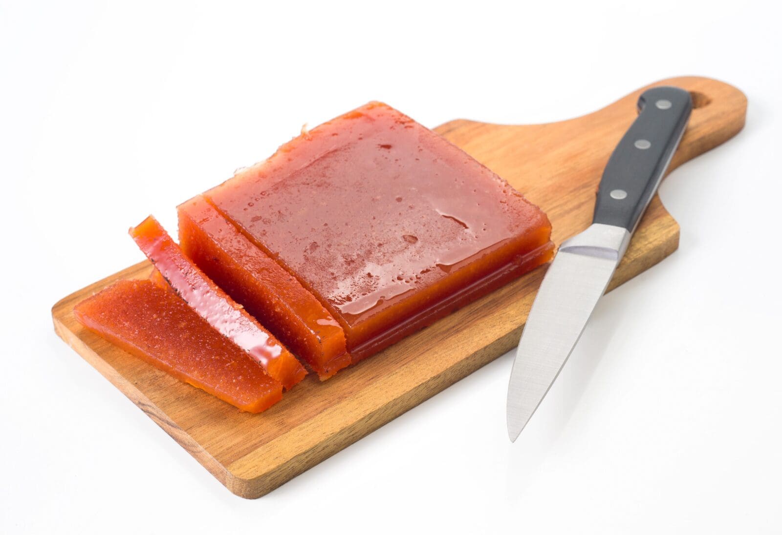 Orange jelly-like block sliced on wooden board with knife beside it.