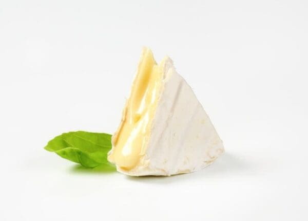 Creamy Cheese with Basil Leaf Wedge of soft cheese with white rind on a surface, with a green basil leaf beside it.