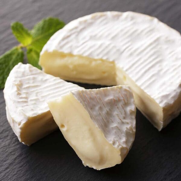Creamy Soft Cheese on Slate Soft cheese with white rind, creamy interior, partially cut on slate with mint sprig.