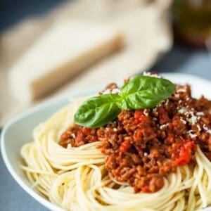 Spaghetti with meat sauce and basil garnish in a white bowl.