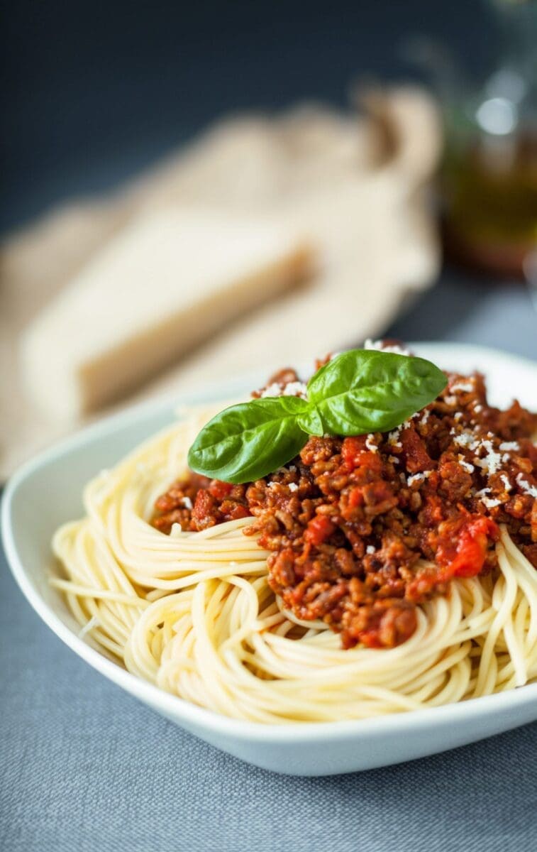 Spaghetti with meat sauce and basil garnish in a white bowl.
