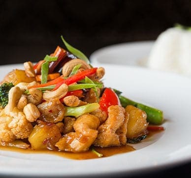 Colorful stir-fried vegetables with cashews on a plate, white rice in the background.