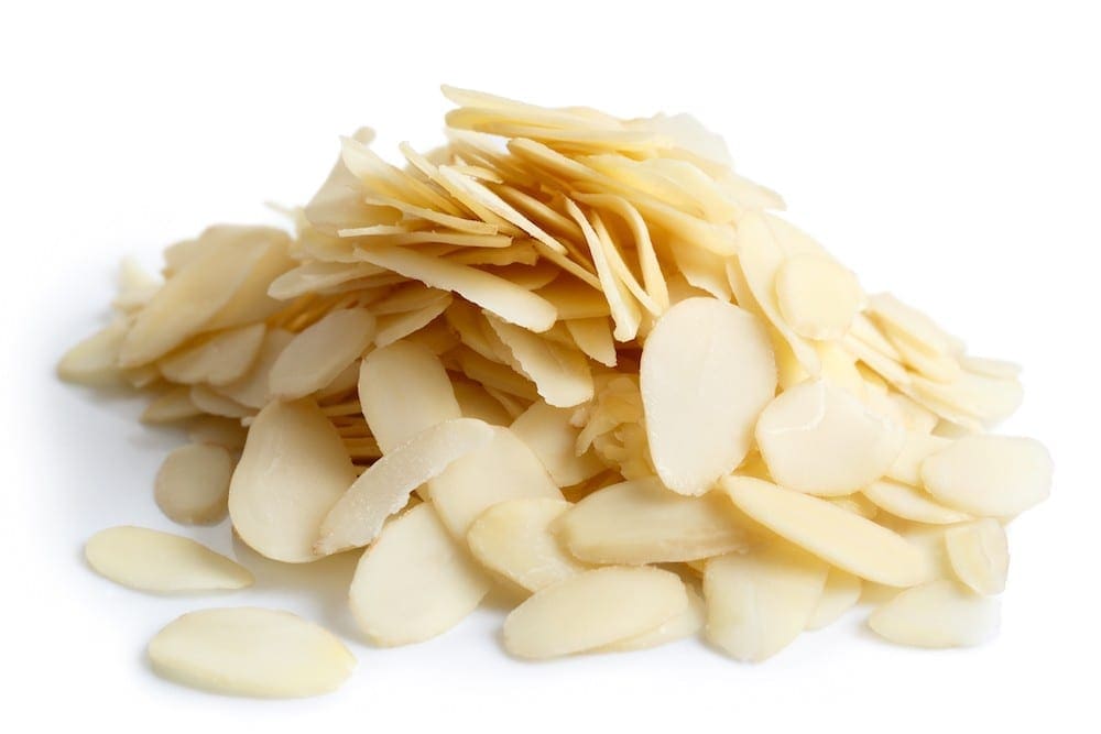 Thinly sliced almonds piled on a white surface, showing creamy color and smooth texture.