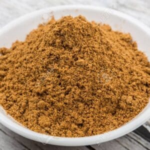 White bowl with light brown ground spice on a wooden surface.