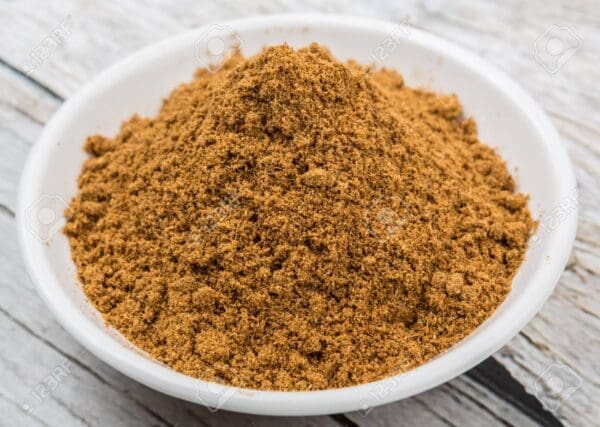 White bowl with light brown ground spice on a wooden surface.