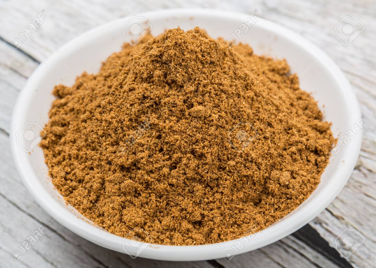 White bowl with light brown ground spice on a wooden surface.