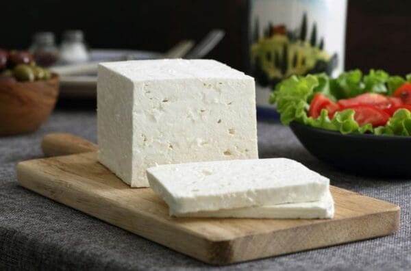 Cheese Block with Salad and Olives White cheese block on cutting board, with salad, olives, and container in the background.